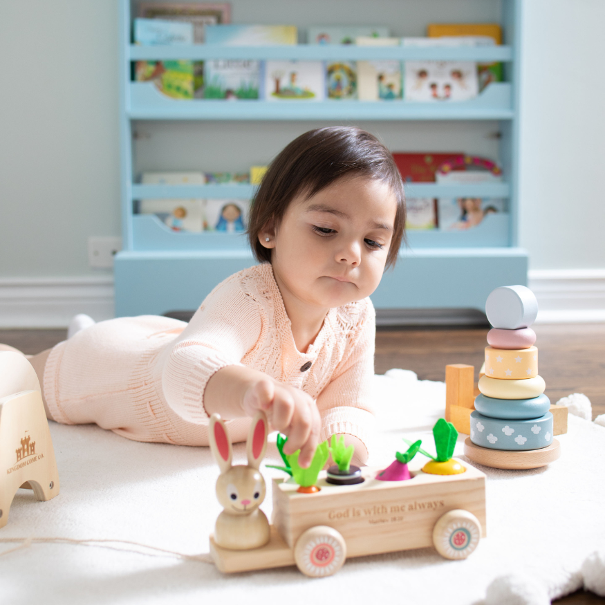 young child playing with wooden heirloom Montessori inspired toys on the floor in front of a blue bookshelf.