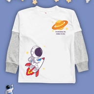 White kids Christian tshirt with gray long sleeve undershirt decorated with an astranaut riding a rocket heading towards a planet with the words 'He determines the number of stars" under it.
