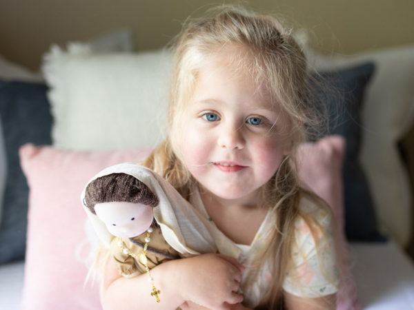 girl looking at camera as she hugs her Blessed Virgin Mary waldorf inspired doll