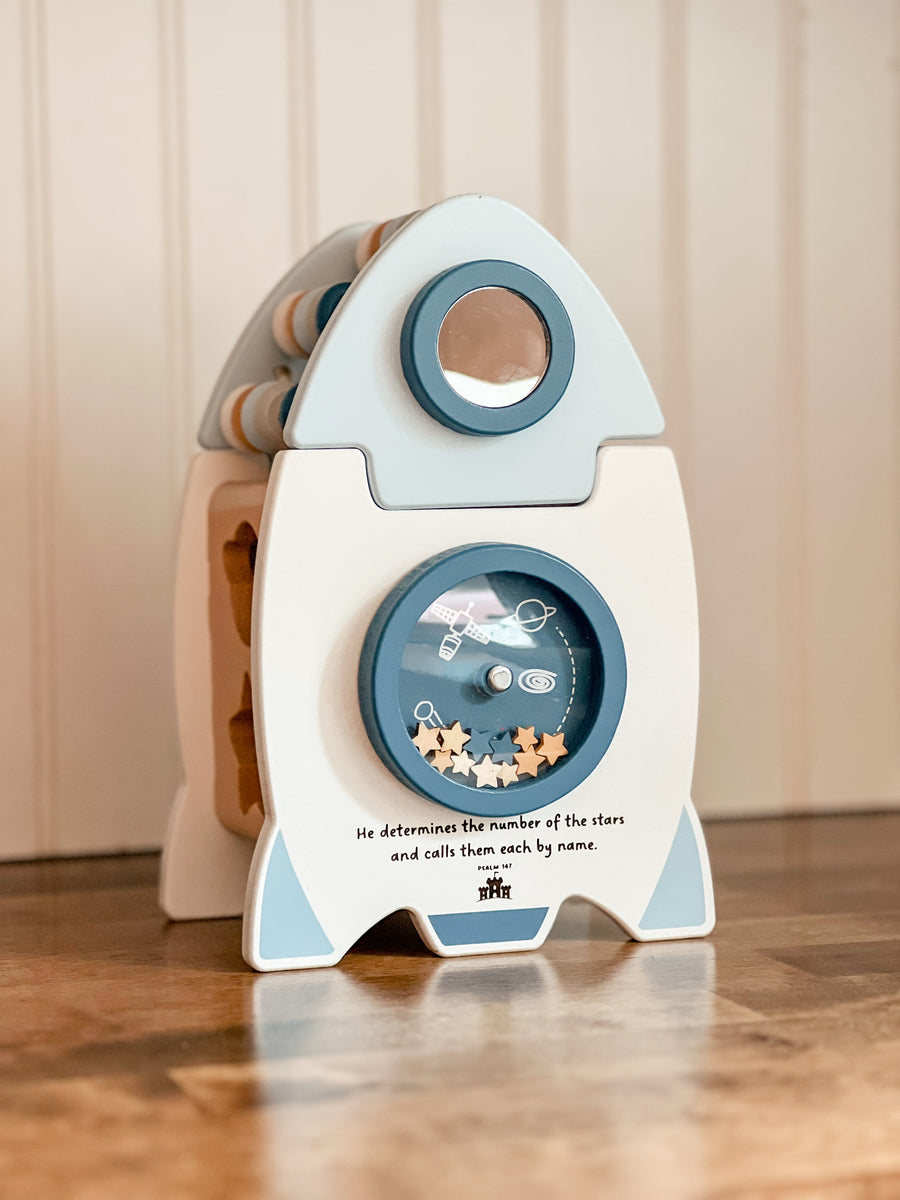 Wooden rocketship shape sorter toy with the verse 'He determines the number of stars and calls them each by name' engraved on the front.